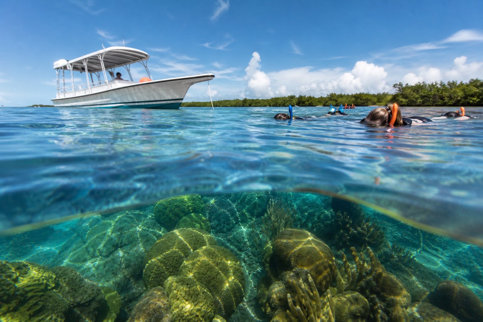 Snorkelers slip into clear water beside a boat over coral reef.
